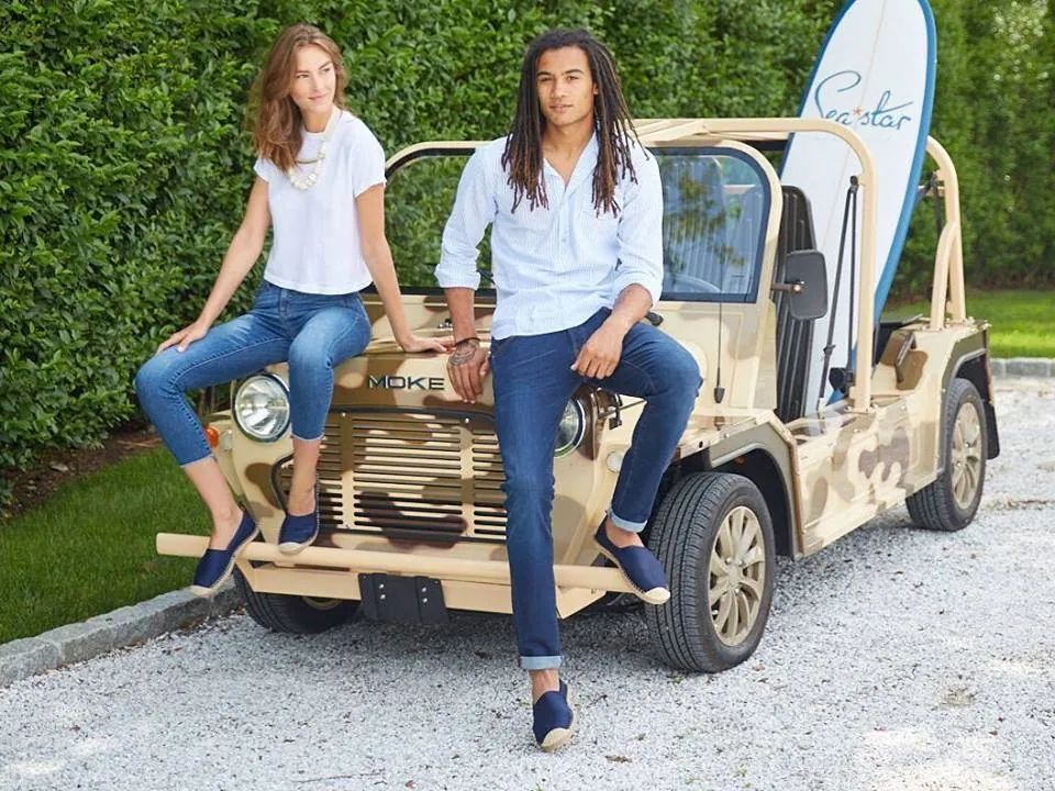 Couple with surfboard sitting on a sand-colored Moke at Sea Star Beachwear